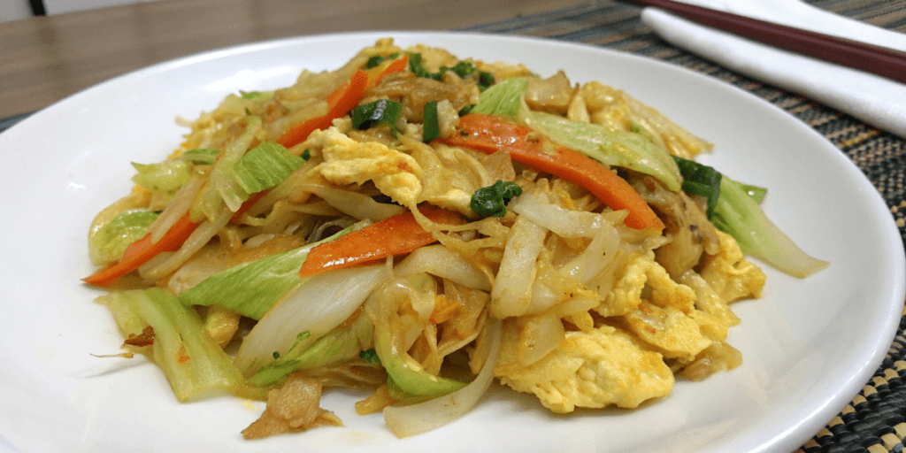 A serving of Cabbage and Egg stir-fry on a white plate, featuring cabbage, scrambled eggs, sliced bell peppers, onions, and other vegetables