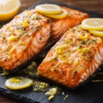 Golden baked lemon garlic salmon fillet with herb seasoning on white plate with lemon slices and fresh parsley